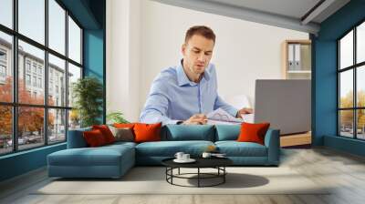 Professional business accountant working in office. Man in shirt sitting at his desk, doing paperwork, working with financial documents, using laptop computer and checking some figures on calculator Wall mural