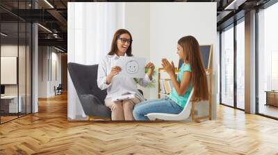 Professional school psychologist talks about positive emotions during meeting with preteen girl. Friendly female counselor shows teenage girl sheet of paper with smiley emoticon drawn on it. Wall mural