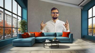 Self assured man wearing funny sunglasses. Studio shot of smirking smug looking student or businessman in white shirt and thug life glasses doing rock sign gesture standing isolated on grey background Wall mural