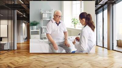 Senior man on check up appointment with young doctor who writing symptoms in flipboard and listening him sitting on the couch. Checkup, prevention examination, tests, diagnosis, medicine concept. Wall mural