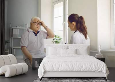 Senior man patient suffering from a headache, sitting on a medical couch, holding hand on his head and telling the doctor about the intense pain that he is feeling. Medicine, medical help concept Wall mural