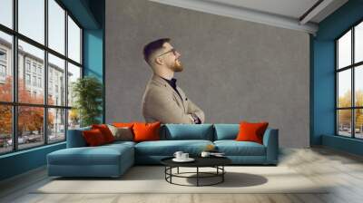 Side view happy man in jacket and glasses standing and looking at text copyspace on grey background. Profile portrait young hipster businessman thinking of interesting idea or good business solution Wall mural