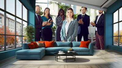 Smiling beautiful female professional leader manager standing looking at camera in office, happy confident business woman corporate leader boss ceo posing, team applauding to support in admire Wall mural