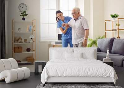 Smiling caregiver helping senior man to stand up and walk. Female nurse assisting her elderly patient suffering from mental disability in nursing home. Disabled old man trying to walk with assistance Wall mural