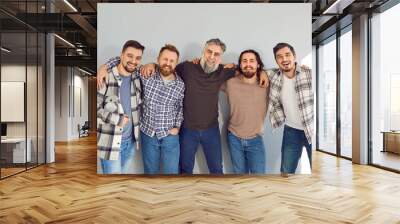 Smiling male friends standing and hugging near gray wall. Portrait of five happy hipster men wearing casual clothes posing for photo at meeting and looking at camera Wall mural