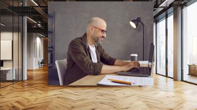 Smiling middle-aged man in spectacles work online on computer consult client in modern home office workplace. Happy male freelancer employee type on laptop, have distant job. Technology concept. Wall mural