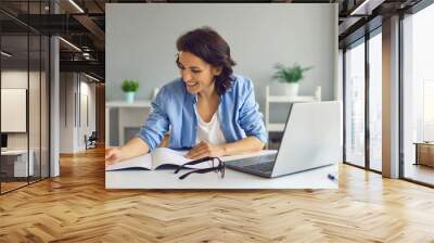 Smiling woman making notes during online lesson or meeting on laptop Wall mural