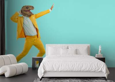 Strange guy in reptile costume dancing and having fun. Crazy young man wearing yellow suit and funny dinosaur mask dancing and moving hands isolated on blank turquoise copy space background Wall mural