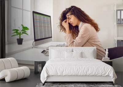 Stressed, tired young woman financial accountant with eye strain and headache holding her nose bridge while sitting at working desk with computer in office. Pain, stress at work, overworking concepts Wall mural