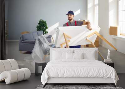 Strong young man from a moving company or truck delivery service carrying a white wooden table while removing furniture from a modern house or apartment Wall mural