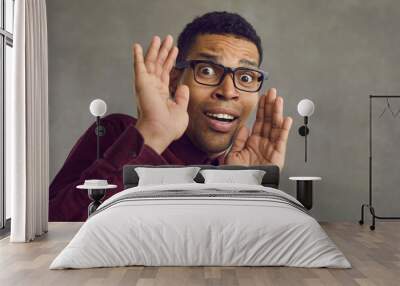 Studio portrait of black man in glasses gasping and panicking scared by something terrible. Shy African American guy afraid of camera looking at it with expression of fear and fright on his young face Wall mural