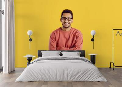 Studio portrait of happy male college or university student. Handsome young black man in glasses standing with his arms folded isolated on color background, smiling and looking at camera Wall mural