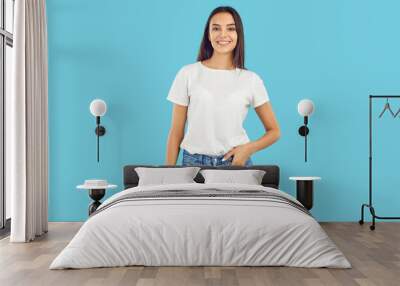 Studio shot of a young female model posing in casual clothes. Happy beautiful woman wearing a white mockup T shirt and comfortable blue jeans standing isolated on a blue background. Fashion concept Wall mural