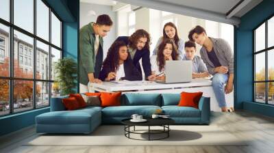 Teacher helping students. Male teacher is using laptop to explain lesson topic to group of college students. Group of students together with the teacher use modern devices for learning. Wall mural