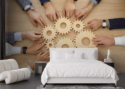 Team of business people join gearwheels. High angle, overhead view of circle of hands holding cogs on office table. Metaphor for good effective business system, cooperation, teamwork and efficiency Wall mural