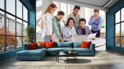 Team of business people using a modern computer during a work meeting in the office. Group of happy diverse men and women looking at the laptop on the desk Wall mural