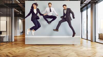 Team of crazy business people having fun in the office. Group of three happy, funny, excited, young employees and colleagues in suits, shirts and ties dancing and jumping together Wall mural