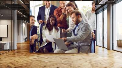 Team of diverse business people meeting in office, working on project and using laptop. Group of young and mature mixed race male and female employees looking at notebook computer all together Wall mural