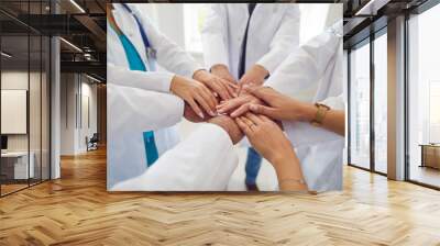 Team of doctors in white uniform standing in hospital or clinic putting their arms in a pile. Stack of medical staff hands. The concept of unity, partnership, teamwork and health care . Wall mural