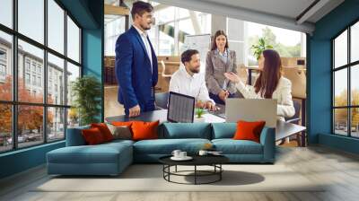 Team of four business people having corporate staff work meeting. Group of friendly young men and women using modern laptops and having discussion at wooden table in cozy office interior Wall mural