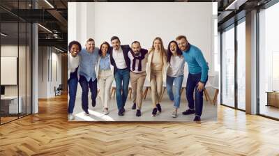 Team of happy mixed race business people having fun in office. Diverse group of young male and female employees and friends standing in row, hugging each other, smiling and laughing. Teamwork concept Wall mural