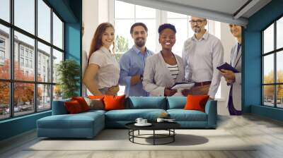 Team of happy successful diverse business people standing in office. Group of six cheerful multiracial employees standing together, holding clipboards, looking at camera and smiling. Banner background Wall mural