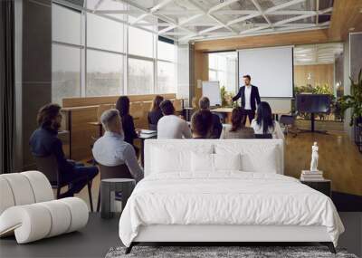 Team of people having class with business trainer. Group of male and female employees sitting at desks in modern office and listening to lecture by experienced teacher sharing knowledge and guidance Wall mural