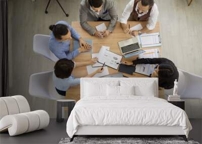 Team of people having important discussion in business meeting. Group of men and women working with sales reports sitting around wooden table in modern office, high angle, view from above, top view Wall mural