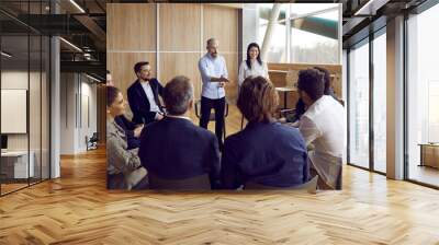 Team of people meeting with business coach. Experienced trainer talking to group of office workers, making convincing speech about motivation and skills, asking questions, sharing knowledge and advice Wall mural