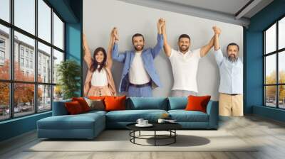 Team of successful business people of different ages holding hands and smiling. Banner with group portrait of happy motivated multi aged men and women standing together against grey studio background Wall mural