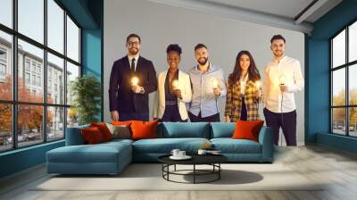 Teamwork and brainstorming, innovation idea creation and share. Diverse interracial business team positive smiling holding glowing light idea bulb standing over grey copy space studio background Wall mural