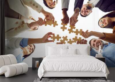 Teamwork. Happy different people put together pieces of wooden puzzles that symbolize teamwork. Smiling young multiracial people stand in circle and each holds one piece of puzzle. Bottom view. Wall mural