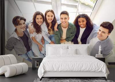 Top view of a group of happy smiling friends high school students standing together and looking cheerful and positively at the camera in hallway. Portrait of friendly people guys and girls indoors. Wall mural