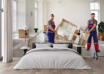 Truck delivery service workers in workwear uniforms removing furniture from house or apartment. Two happy young men from moving company carrying bookshelf together Wall mural