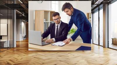 Two business people in suits meet in office, talk, use laptop and work with documents. Man who has some difficulty with interpreting legal agreement is consulting with colleague and asking questions Wall mural