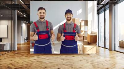 Two happy truck delivery or moving company workers guarantee best service. Portrait of young men in uniform workwear standing in living room or office, looking at camera, showing thumbs up and smiling Wall mural