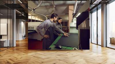 Two shoe factory workers standing at cutting machine at workshop and discussing quality of black leather material for future boots. Using automatic equipment in footwear manufacturing industry concept Wall mural