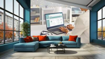 Woman enjoys online banking for work, business or personal needs. Businesswoman or remote worker sitting at desk at home, using laptop computer, managing her bank account and transferring money online Wall mural