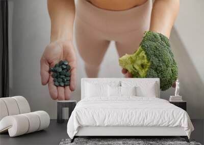 Woman holding fresh broccoli head and spirulina pills before making healthy smoothie Wall mural