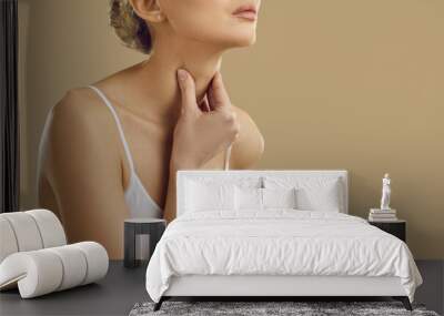 Woman suffering from sore throat, difficulty swallowing and loss of voice on beige background. Cropped image close up of young woman holding her neck near copy space. Healthcare and medical. Banner. Wall mural