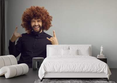 Yeah. Portrait of crazy cheerful businessman having fun on copy space background. Grey ad copyspace banner with funny handsome man with curly Afro hair doing horn sign and laughing. Rock party concept Wall mural