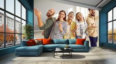 Young, cheerful and funny friends with microphone sing loudly and laugh while playing karaoke at home party. Close up of people in casual clothes. Concept of friendship, home entertainment and people. Wall mural