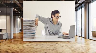 Young accountant working on laptop computer sitting at desk with pile of papers. Paperwork vs electronic documents. Storing files in digital database. Having quick convenient access to storage system Wall mural