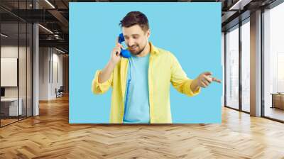 Young Caucasian man isolated on blue studio background talk on landline telephone. Male client have conversation on corded phone with customer service support. Telecommunication concept. Wall mural