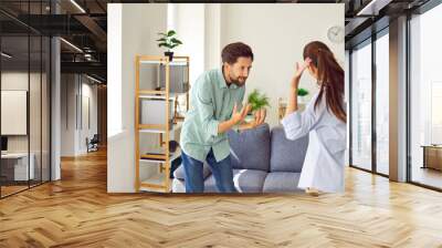 Young couple man and woman standing at home and arguing shouting in quarrel. Angry unhappy husband and wife quarreling in the living room. Marriage problems, relationship and divorce concept. Wall mural