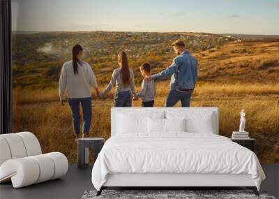 Young family of four with son and daughter walking outdoors enjoying beautiful nature. Happy parents mother, father with two children having a walk in the field together. Family leisure concept. Wall mural