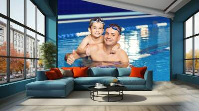 Young father and his little son having fun in an indoor swimming pool. Wall mural