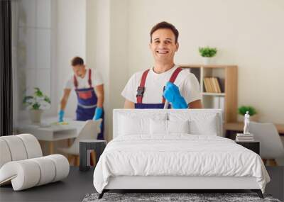 Young male cleaner in overall, happy smiling man performing cleaning duties, professional team busy sanitizing, sweeping, polishing, mopping floor, house cleaning services for home, office Wall mural