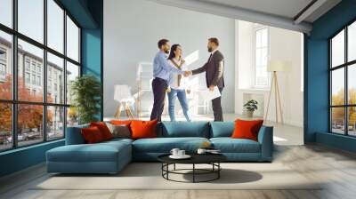 Young married couple make deal, buy new house and exchange handshake with relator. Happy man and woman standing in modern light spacious light living room and shaking hands with real estate agent Wall mural