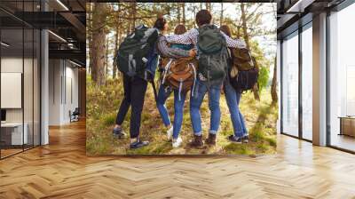 Young people with backpacks stand in the forest from behind. Wall mural